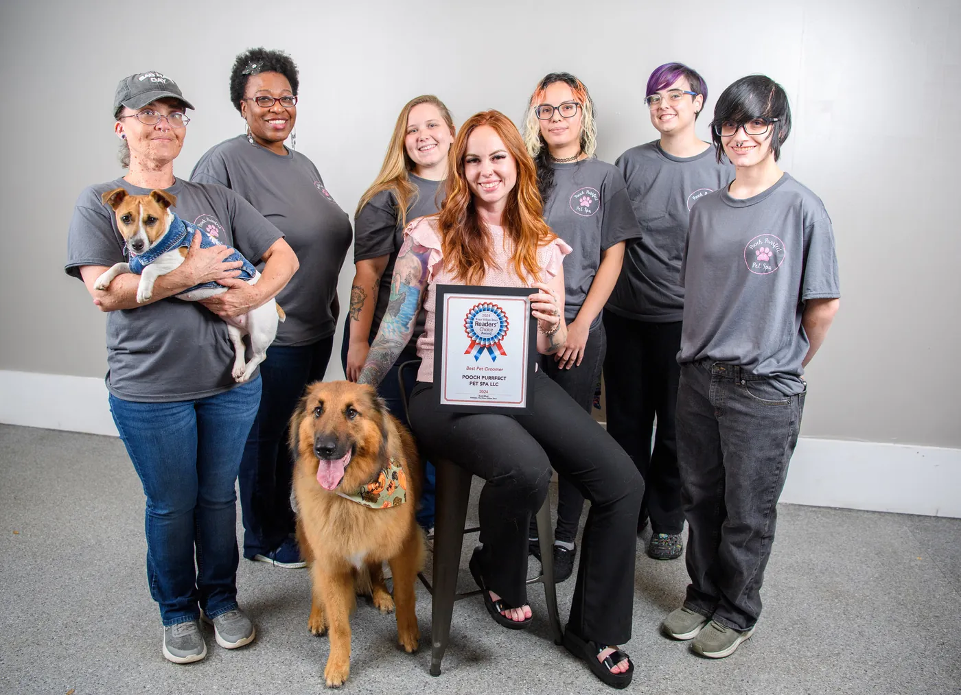 The Pooch Purrfect Pet Spa team in matching gray shirts with two dogs, holding the 2024 Readers' Choice plaque for Best Pet Groomer